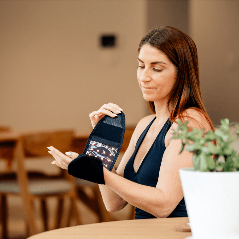 a woman using a red light mini wrap on her wrist