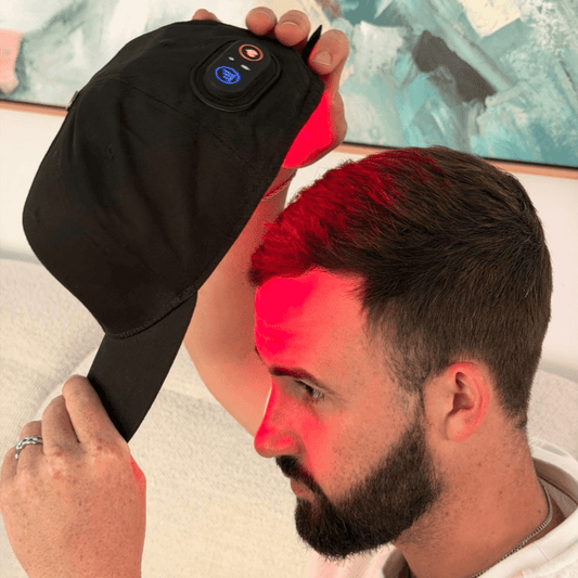 Side view of a man holding the EliteRelief red light therapy cap above his head with red light across his scalp
