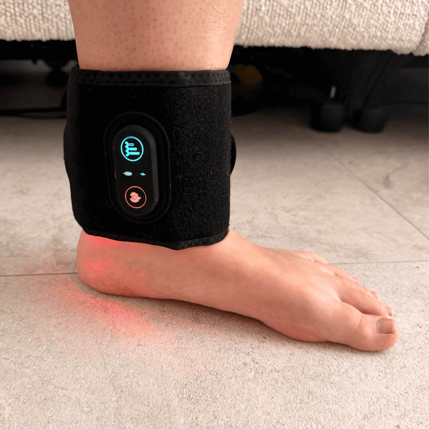 Person wearing a red light therapy device on their ankle with digital display on a light-colored floor.