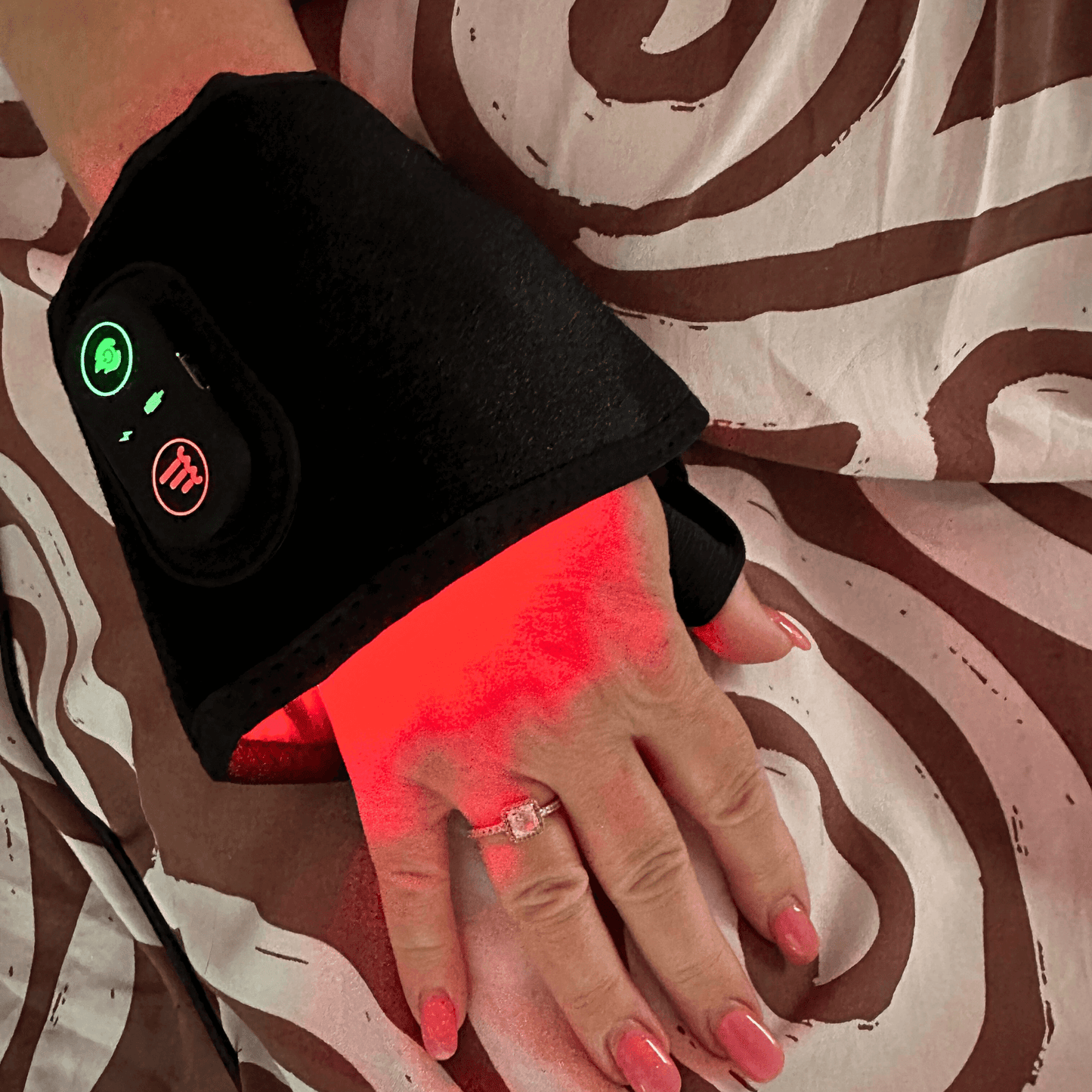 Hand wearing a Red Light Flex Wrap device on their wrist with a patterned fabric background
